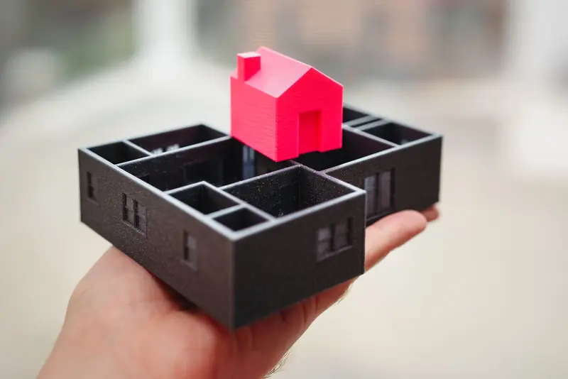 A hand holding a 3D printed model of a house and floor plan, showcasing architectural design