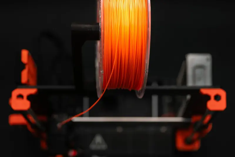 Close-up of an orange 3D printer filament spool in a workshop setting, highlighting innovation and design