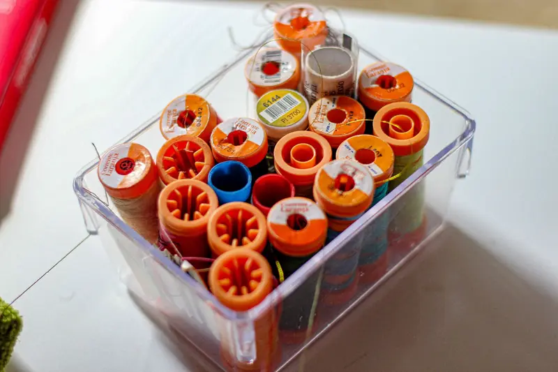 Close-up of assorted colorful thread spools stored neatly in a transparent container
