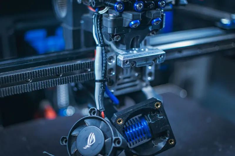Detailed view of a 3D printer showcasing components like wires, gears, and cooling fan