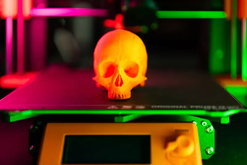Close-up of an orange 3D-printed skull on a 3D printer with vibrant lighting