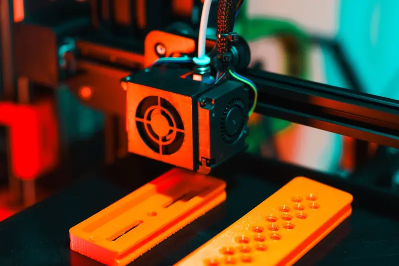 Detailed view of a 3D printer in action, extruding orange plastic components