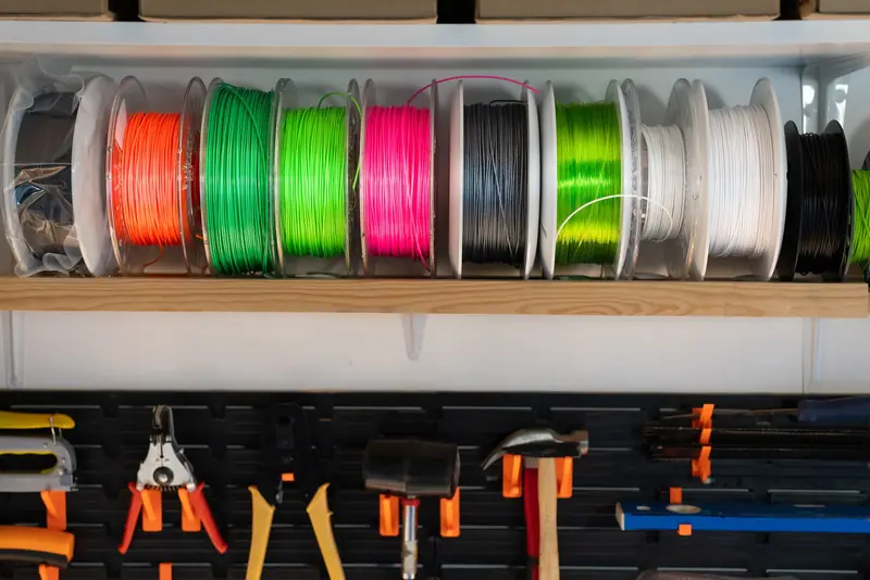 A variety of colorful filament spools and tools organized on a workshop shelf, ideal for 3D printing enthusiasts