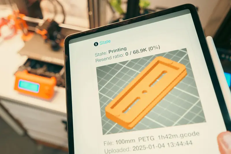 Close-up of a digital tablet displaying a 3D printing process in a workshop setting
