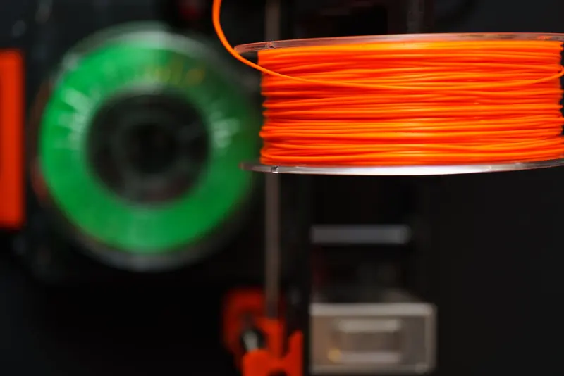 Detailed view of orange and green 3D printer filament spools, perfect for creative and industrial projects